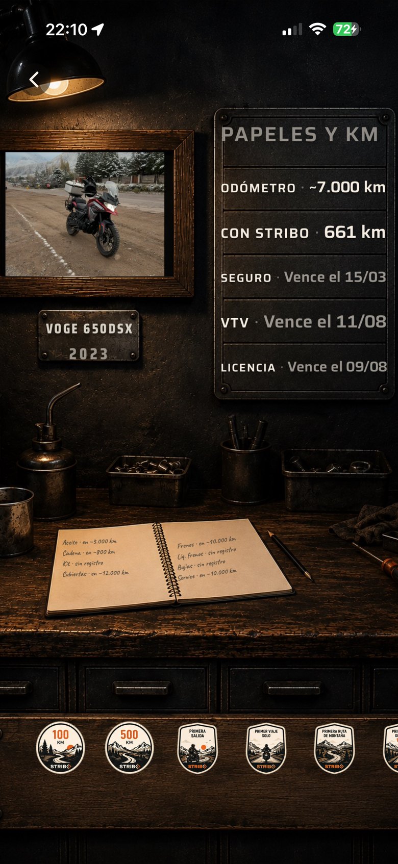 La escena real del taller: la moto enmarcada, la chapa con los datos, el cuaderno de mantenimiento manuscrito y el tablón de insignias